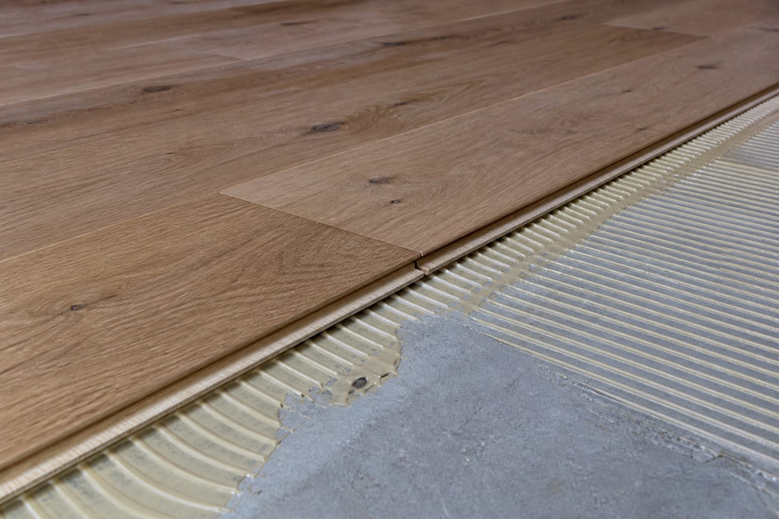 Glue-down engineered hardwood planks being installed on a concrete subfloor